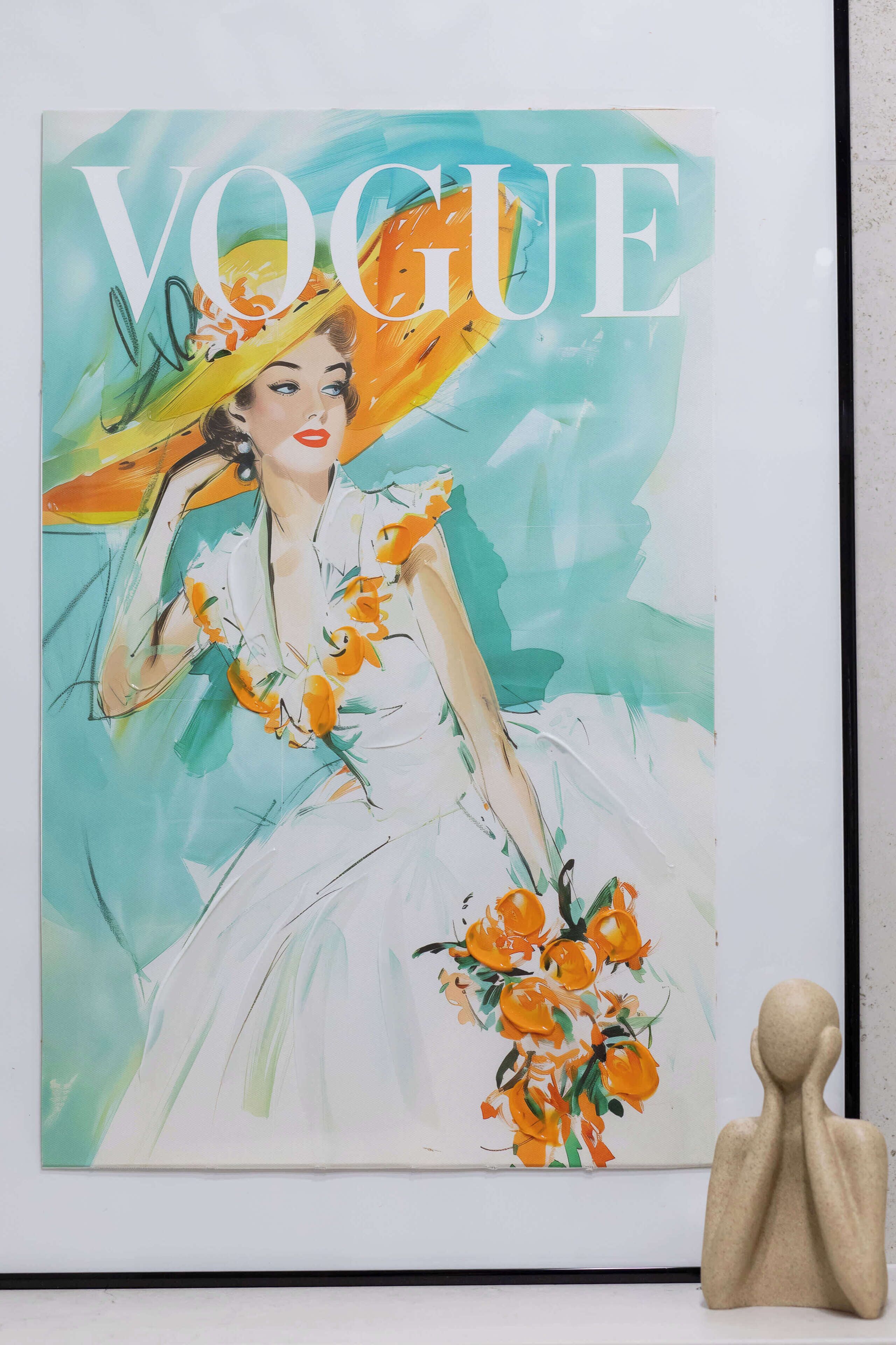 A framed artwork with the word 'VOGUE' prominently displayed, featuring a person in a white dress holding a bouquet of flowers.