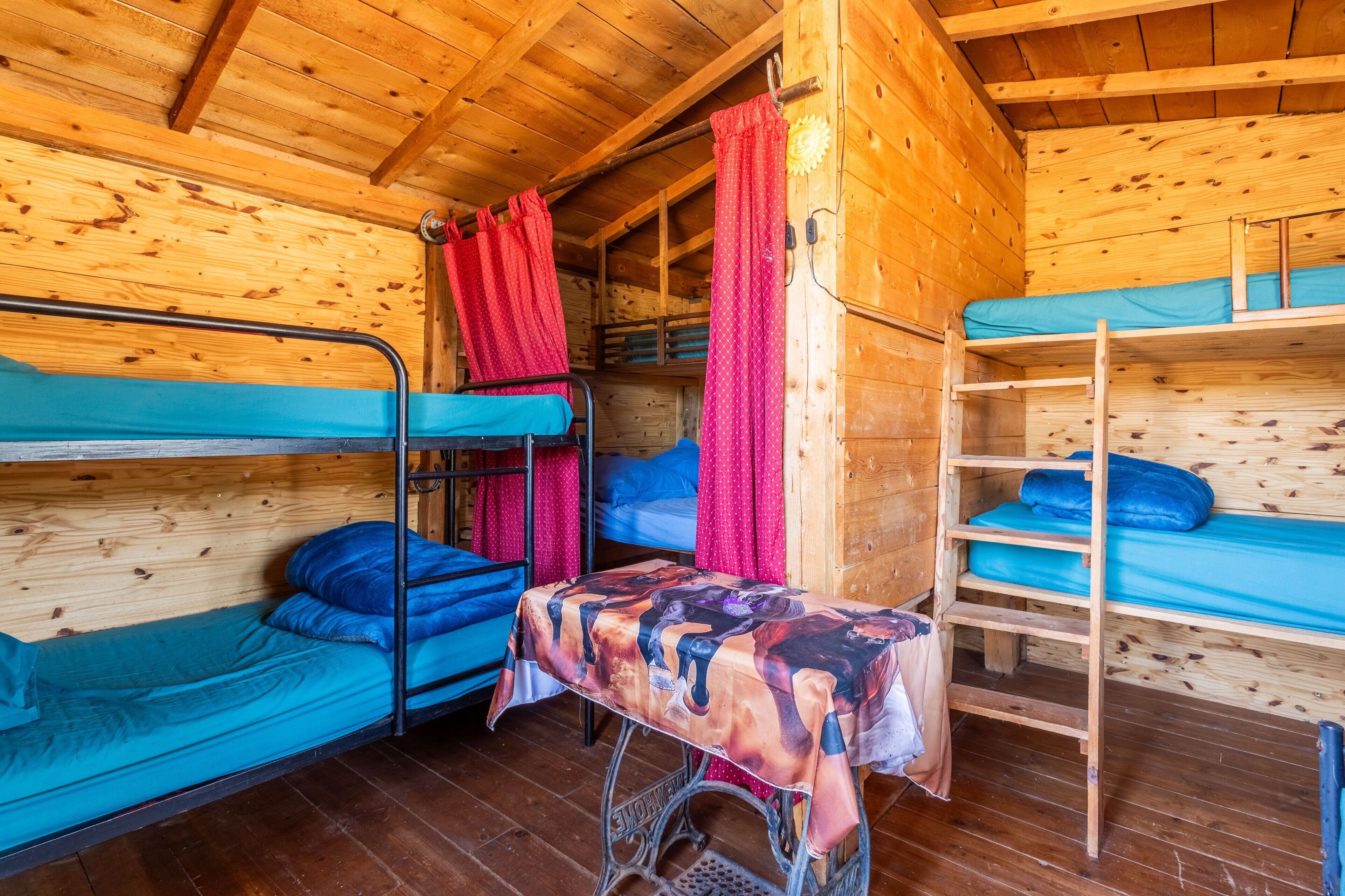 Una cabaña de madera con literas, una mesa con mantel y una cortina roja.