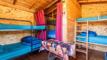 Eine Holzhütte mit Etagenbetten, einem Tisch mit Tischdecke und einem roten Vorhang.