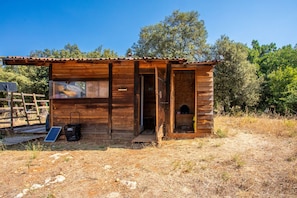 A wooden cabin with a door leading to an interior space, a small porch area, and a solar panel on the ground.