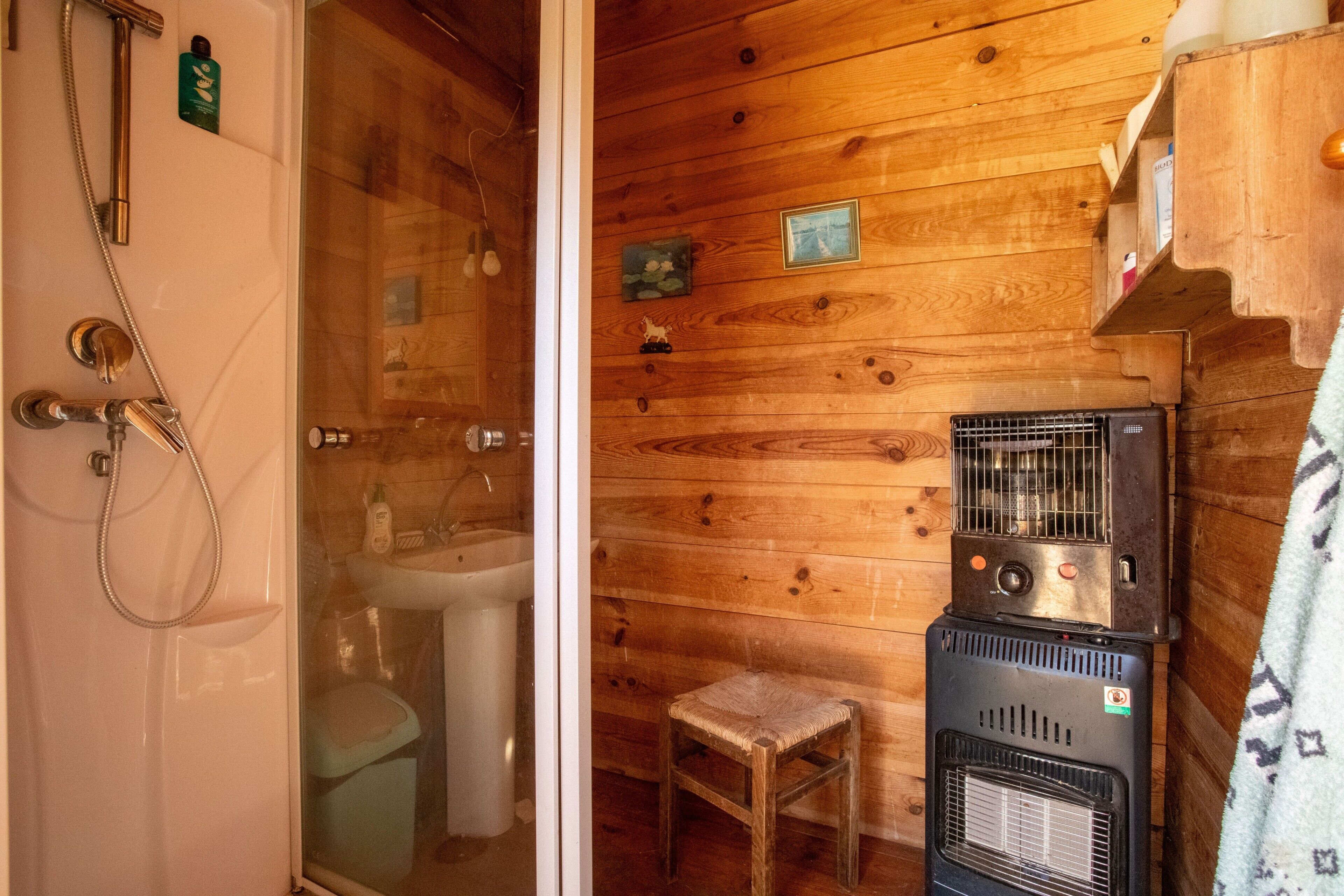 A wooden cabin bathroom with a glass shower enclosure, a sink, a toilet, and a small wooden stool.