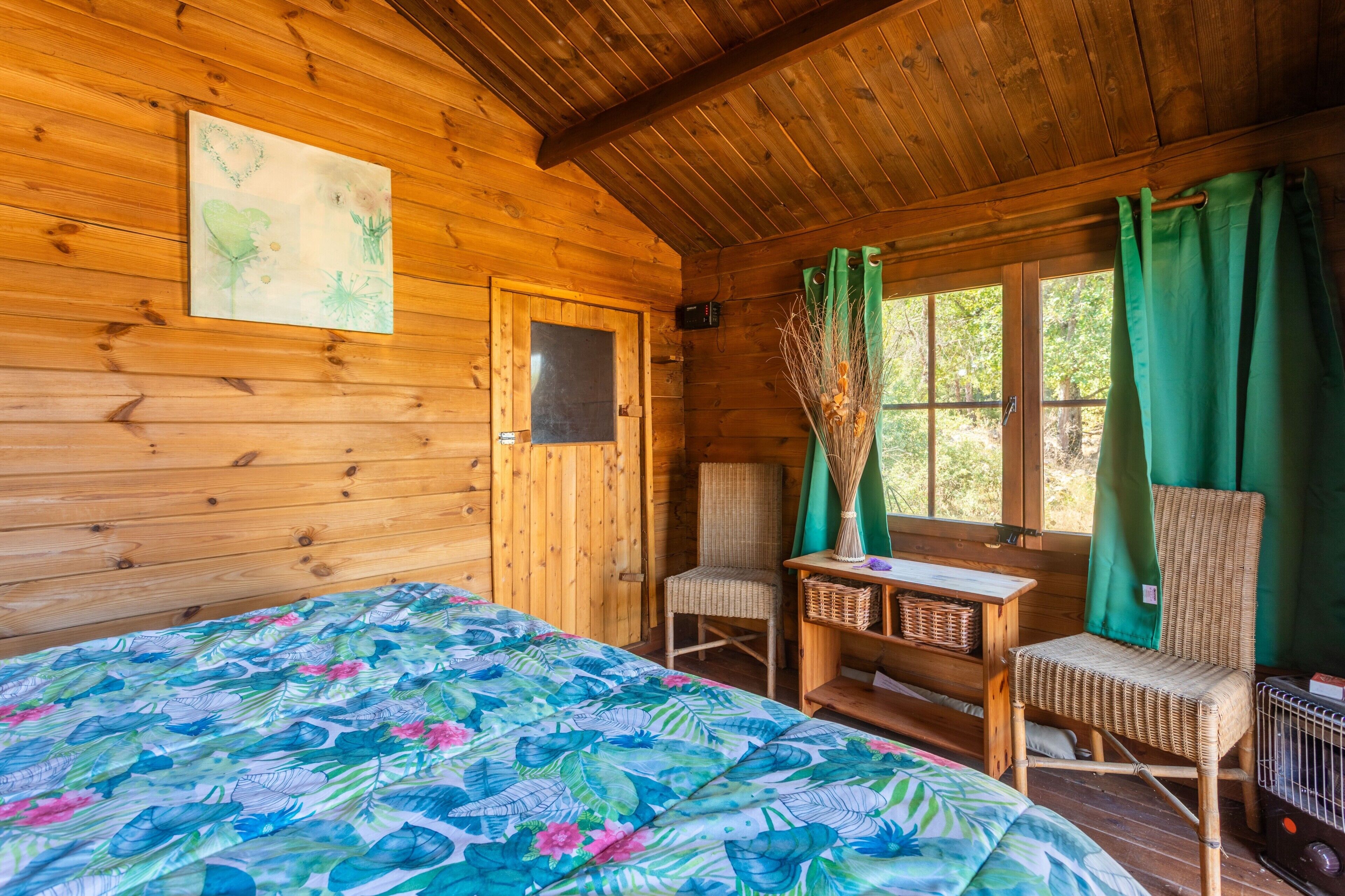 Una habitación de cabaña de madera con cama, dos sillas, una mesita y una ventana con cortinas.