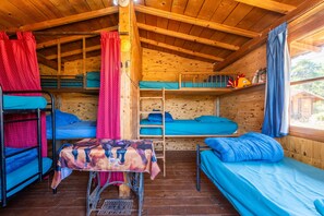A cabin with bunk beds, a table with a patterned tablecloth, and a window with curtains.