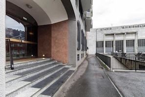 A building with a staircase leading to a covered entrance, a balcony with a railing, and a sign that reads 'STADIO G.SINIGAGLIA'. - [Lungolago] Nuovo Bilocale 5 (Como)