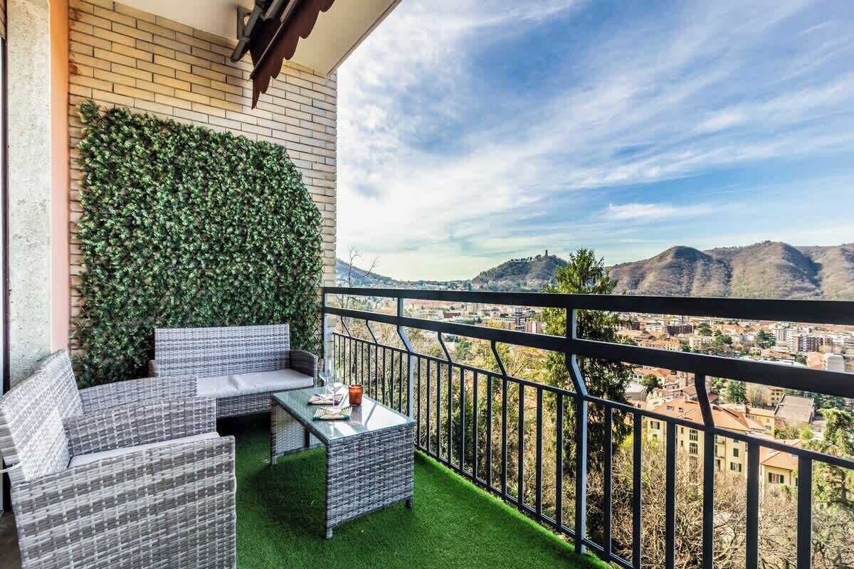 Un balcon offrant une vue sur la ville et les montagnes, aménagé avec des meubles en osier et une petite table.