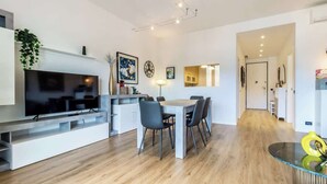 A modern living space with a flat-screen TV, dining table, chairs, and a kitchen area. - silk and sunset - city and lake view (Como)
