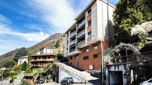 A multi-story building with balconies, a parking area, and a hillside backdrop. - silk and sunset - city and lake view (Como)