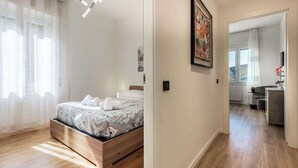 A bedroom with a wooden bed, a large window with sheer curtains, and a hallway leading to a bathroom. - silk and sunset - city and lake view (Como)
