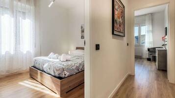 Una camera da letto con un letto in legno, un'ampia finestra con tende leggere e un corridoio che conduce al bagno.