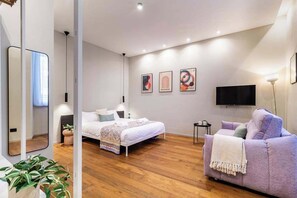 Ein modernes Schlafzimmer mit einem Bett, einer Couch, einem Fernseher und Kunstwerken an der Wand.