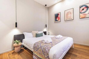 Ein modernes Hotelzimmer mit einem großen Bett, einem Nachttisch, einer Topfpflanze und Bildern an der Wand.