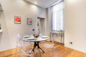 A dining area with a round table, clear chairs, and a bowl of fruit. There are two framed pictures on the wall. - luxury house - como lake - [parcheggio interno] (Como)