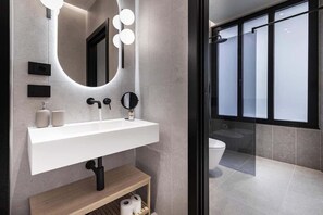 Un baño moderno con un lavabo blanco, un espejo con luces redondas y una cabina de ducha de vidrio.