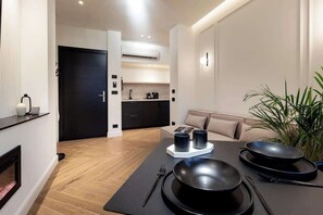 A modern kitchen with black cabinets, a dining area with a black table, and a sofa. - [Lungolago] Nuovo Bilocale 3 (Como)