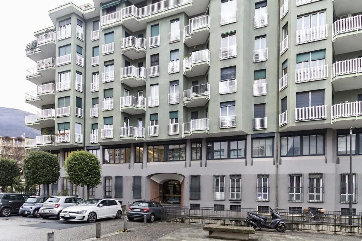 Ein mehrstöckiges Wohngebäude mit Balkonen, parkenden Autos und blauem Himmel.
