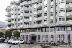 A multi-story residential building with balconies, parked cars, and a clear sky. - [Lungolago] Nuovo Bilocale 3 (Como)