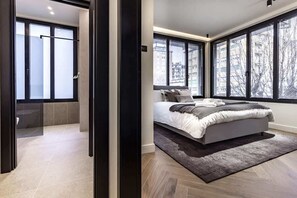 Een moderne slaapkamer met een groot bed, uitzicht op de stad door grote ramen, en een apart badkamergedeelte.