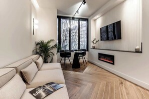 Een moderne woonkamer met een bank, een eettafel met stoelen, een open haard en een aan de muur bevestigde televisie.