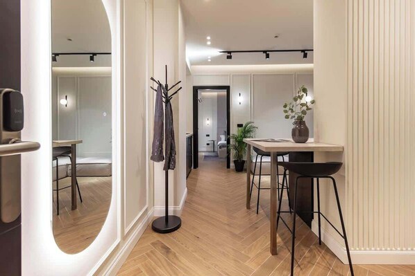 A modern interior with a wooden floor, a dining area with a table and chairs, a coat rack, and a potted plant. - [Lungolago] Nuovo Bilocale 1 (Como)