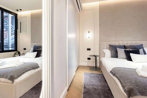 A modern hotel room with two beds, a small round table, and a large window with a city view. - [Lungolago] Nuovo Bilocale 1 (Como)