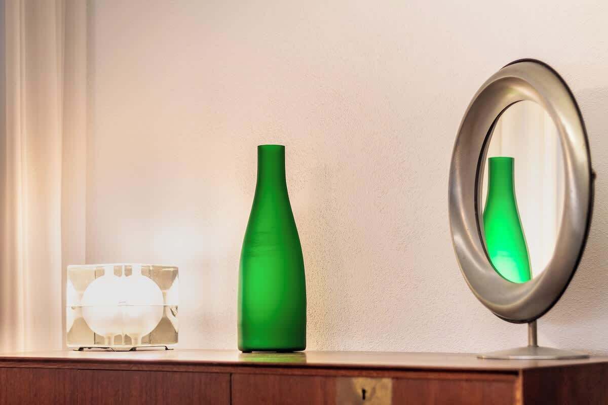 A bathroom vanity with a mirror, a green vase, and a clear glass container.