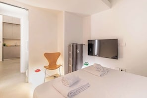 Et moderne hotelværelse med seng, fjernsyn hængt på væggen, en radiator og en stol.
