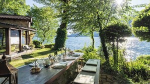 An outdoor dining area with a view of a lake, a pergola, and a stone table set for a meal. - Private Villa Pied en l'eau [Only by Boat] (Riva)