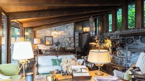 A cozy living room with a fireplace, stone walls, and a dining area with wooden furniture. - Private Villa Pied en l'eau [Only by Boat] (Riva)