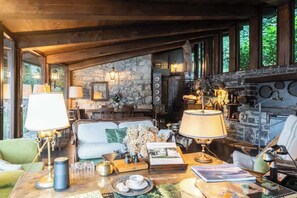 A cozy living room with a fireplace, stone walls, and a dining area with wooden furniture. - Private Villa Pied en l'eau [Only by Boat] (Riva)