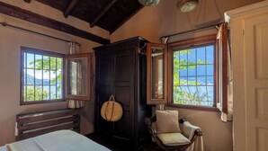 A room with a bed, a dark wooden wardrobe, a chair, and two windows with a view of greenery and a body of water. - Private Villa Pied en l'eau [Only by Boat] (Riva)