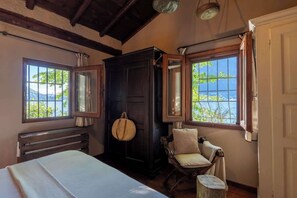 A room with a bed, a dark wooden wardrobe, a chair, and two windows with a view of greenery and a body of water. - Private Villa Pied en l'eau [Only by Boat] (Riva)
