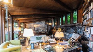 A cozy interior with a stone fireplace, wooden ceiling beams, and a bookshelf filled with books. - Private Villa Pied en l'eau [Only by Boat] (Riva)