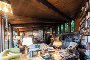 A cozy interior with a stone fireplace, wooden ceiling beams, and a bookshelf filled with books. - Private Villa Pied en l'eau [Only by Boat] (Riva)