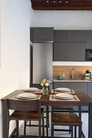 A modern kitchen with dark cabinetry, a wooden dining table set for four, and a vase with flowers on the table. - [Borgovico] Modern Romantic Como Central Apt (Como)