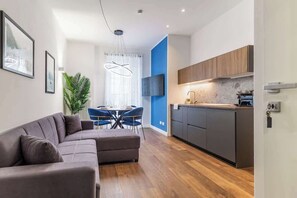 A modern living room with a sofa, dining table, and chairs. There is a kitchen area with cabinets and a countertop. - [Lungolago] Nuovo Bilocale 6 (Como)