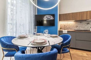 Een moderne eetruimte met een ronde tafel, blauwe stoelen en een flatscreen televisie die aan een blauwe wand is bevestigd.