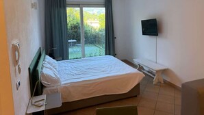 A hotel room with a bed, a television, a bench, and a sliding glass door to the outside.