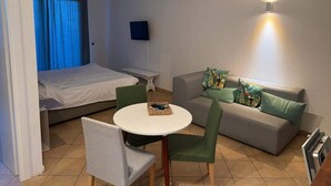 A compact room with a bed, a sofa, a small table, and a TV.