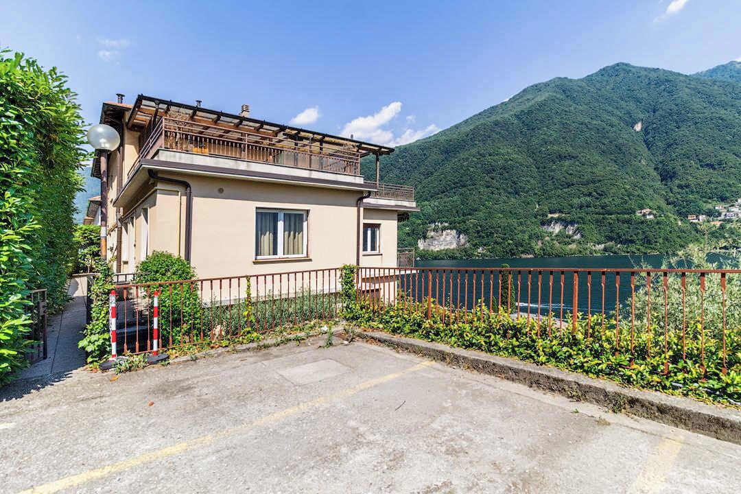 A two-story building with a balcony, surrounded by greenery and a mountain backdrop.