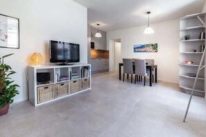 A modern living room with a flat-screen TV, a bookshelf, a dining area with chairs, and a kitchen in the background. - La Bréva - Central Apartment [1 minuto dal centro] (Como)