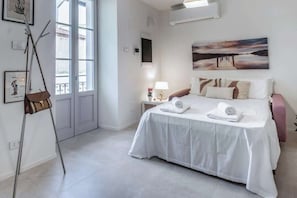 Ein Hotelzimmer mit Bett, Nachttisch mit Lampe, einem Bild an der Wand und einem Fenster.