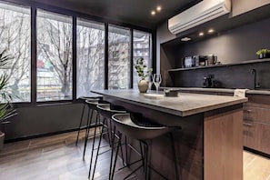 A modern kitchen with a bar area, large windows, and a view of the city. - [Lungolago] Nuovo Bilocale 2 (Como)
