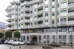 A multi-story residential building with balconies, parked cars, and a bicycle. - [Lungolago] Nuovo Bilocale 2 (Como)