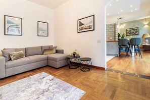 Ein Wohnzimmer mit einer Couch, zwei Beistelltischen und einem Teppich. An den Wänden hängen gerahmte Bilder.