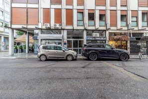 Straßenansicht mit zwei geparkten Autos, einem Gebäude mit der Aufschrift 'CAFFEU' und einem weiteren Schild mit 'PRESTIGE'.