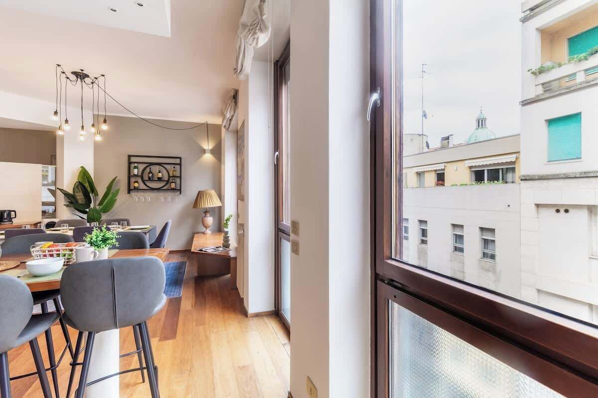 A modern apartment with a dining area, a kitchen, and a large window offering a city view.