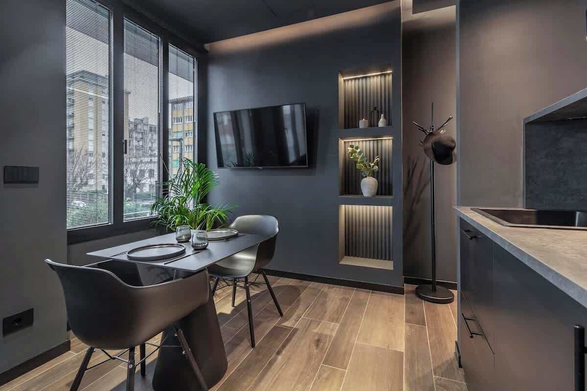 Une cuisine moderne dotée d’un téléviseur encastré, d’un coin repas avec une table et des chaises, et d’une plante.