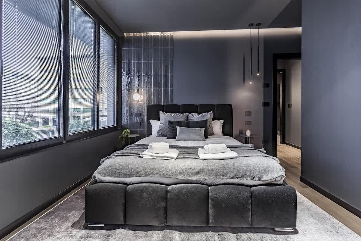 Une chambre moderne avec un grand lit, une décoration aux couleurs sombres et une vue par la fenêtre.