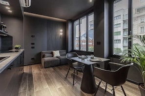 Une cuisine moderne dotée d’une cuisinière intégrée, d’un coin repas avec une table et des chaises, et d’une grande fenêtre avec des stores.