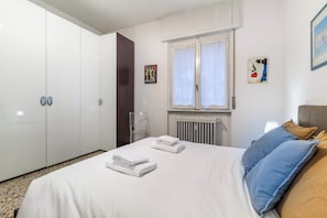A hotel room with a bed, a radiator, a window with curtains, a chair, and a wardrobe. - Casa Franca: Relaxing Como Stay with Mountain View (Como)